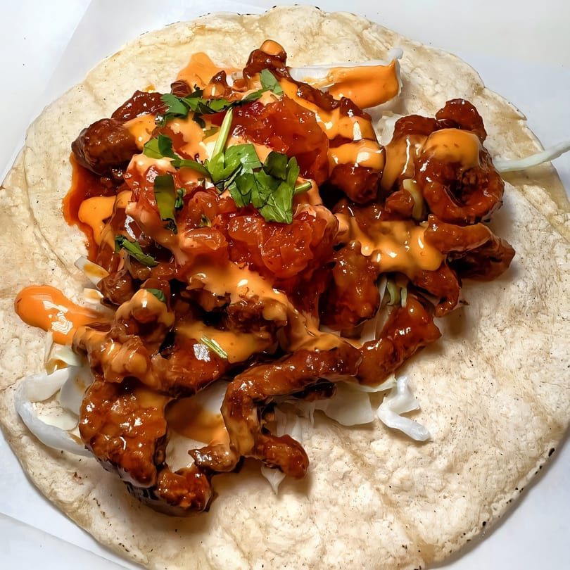 A Korean-Mexican taco with saucy meat, shredded cabbage, and cilantro on a tortilla.