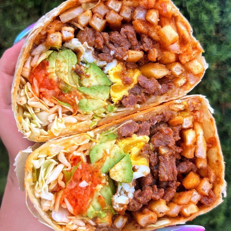 A BOPJO Korean-Mexican Grill burrito, cut in half, revealing beef, fries, avocado, kimchi, and cabbage.
