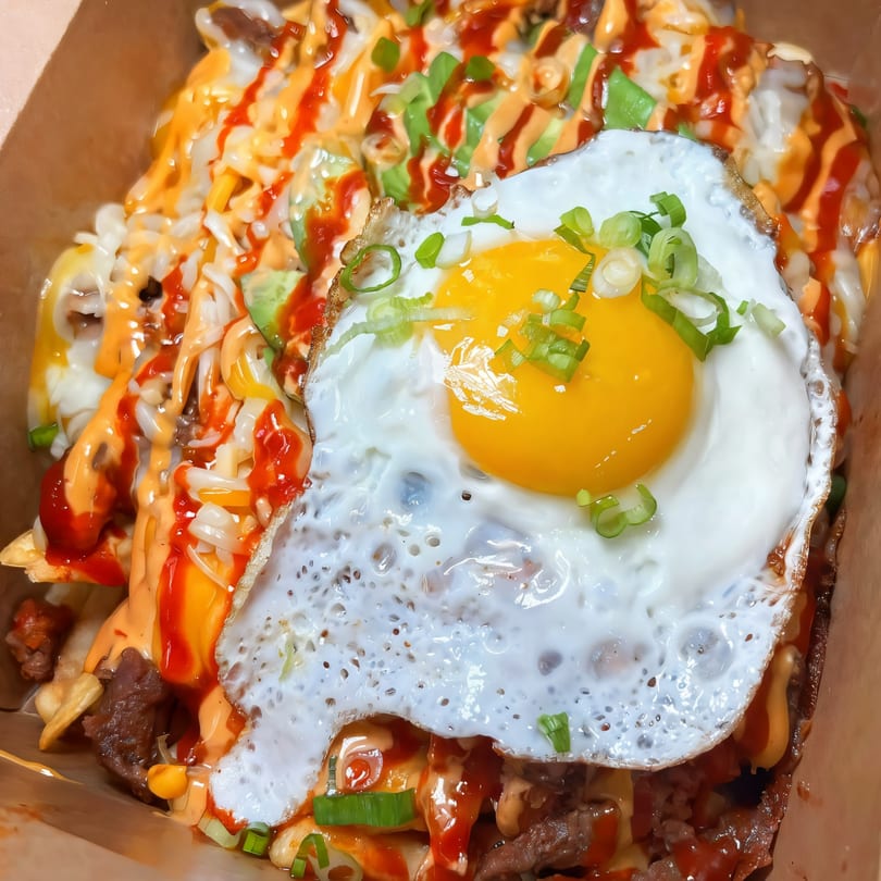 Close-up of BOPJO Korean-Mexican Grill's fries topped with meat, sauces, and a fried egg.