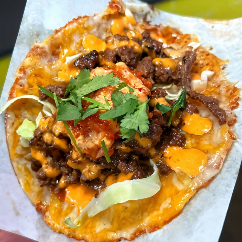 A close-up of a Korean-Mexican taco with meat, cheese, sauce, and cilantro on a tortilla.