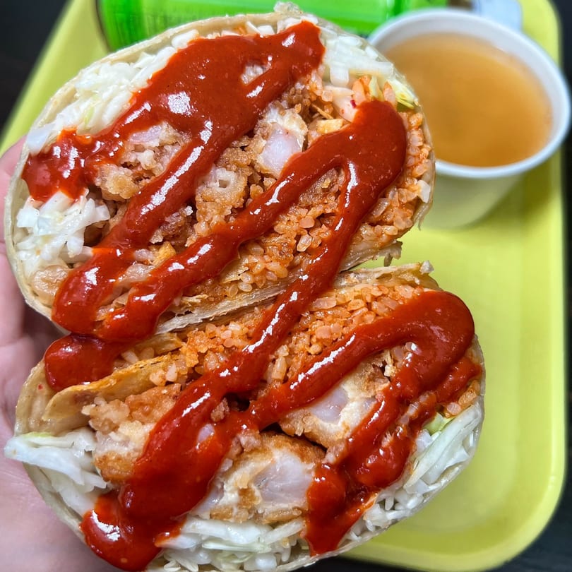 Two halves of a Korean-Mexican burrito, filled with fried chicken, rice, cabbage, and red sauce.